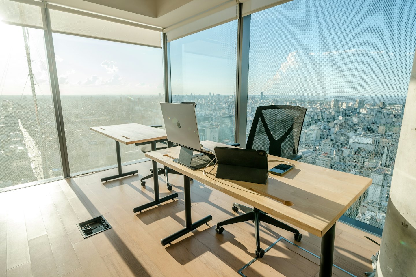 Modern office desks with laptops facing a city skyline.